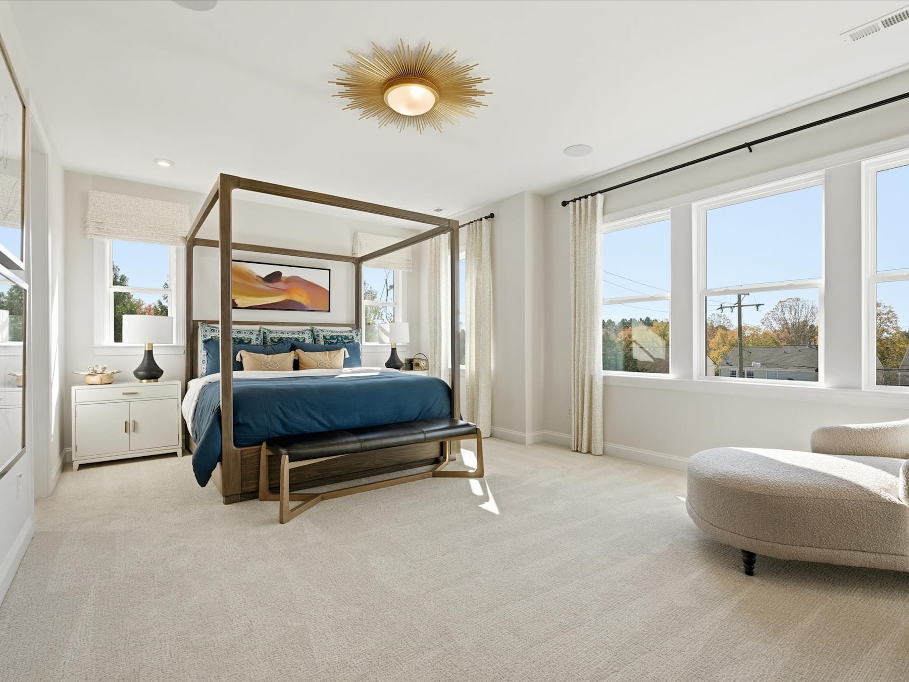 A spacious and modern bedroom with a large bed frame, neutral-toned decor, and a scenic view through the windows.