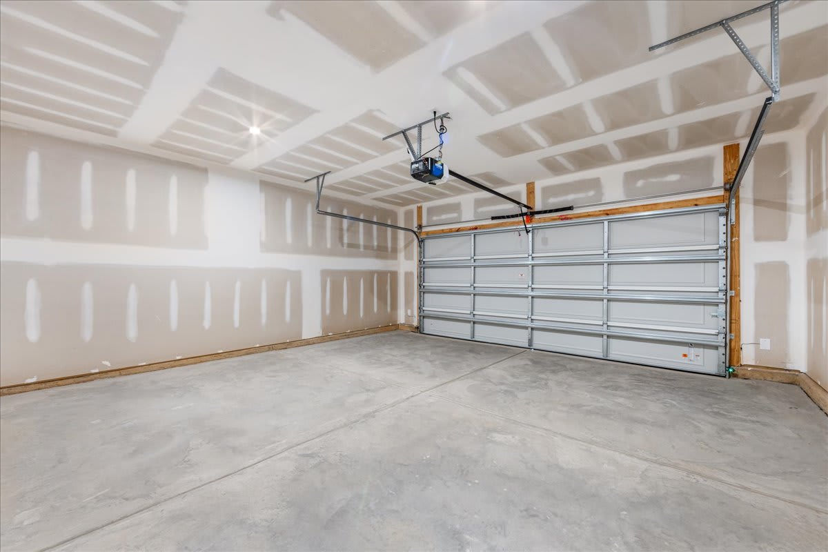 An empty garage interior with a concrete floor, white walls, and a large overhead garage door.