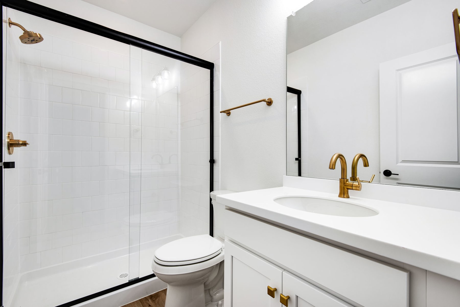 A modern, minimalist bathroom with white walls, a white vanity, and gold fixtures, including a faucet and shower head.