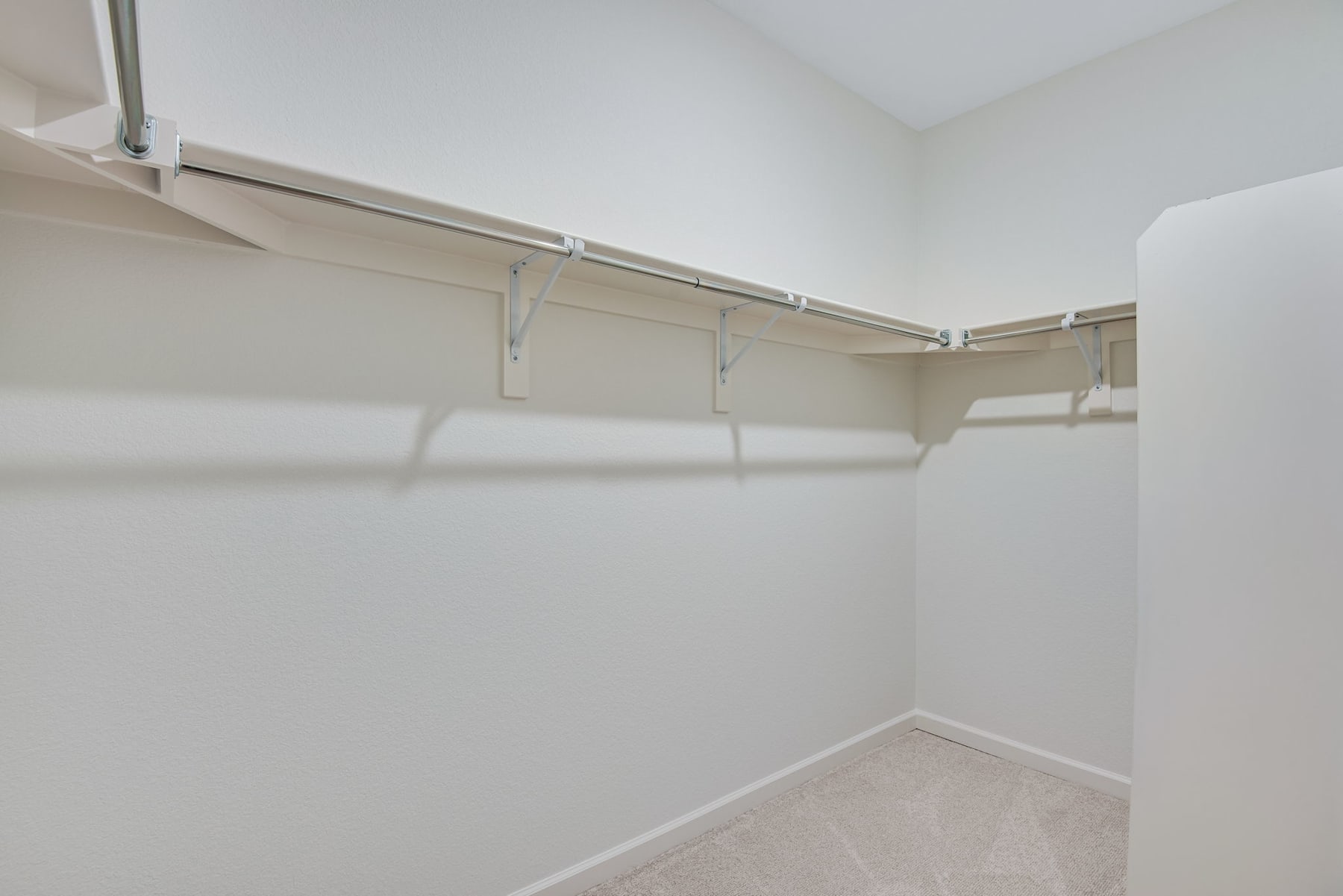 A simple, minimalist closet space with white walls, a metal hanging rod, and a tiled floor.