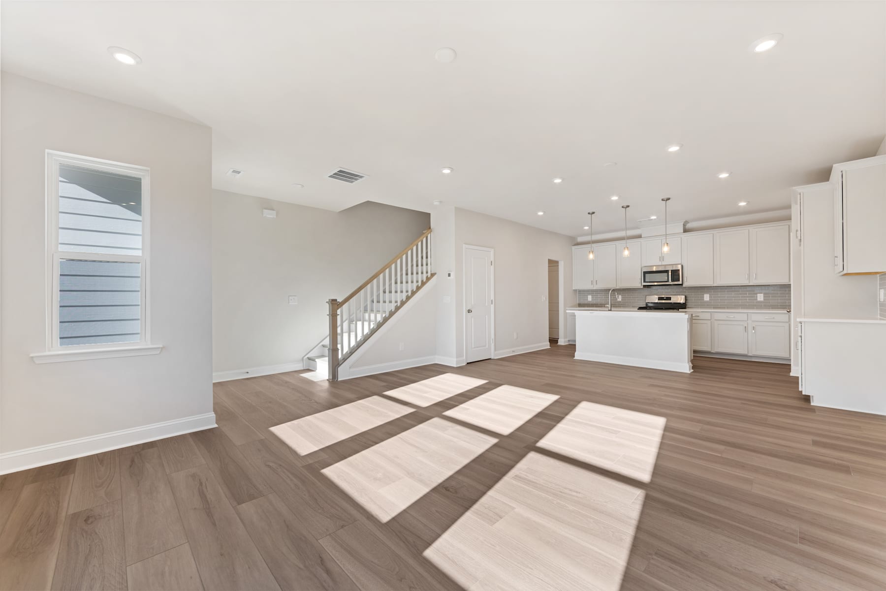 A spacious and modern open-plan living area with a kitchen, hardwood floors, and natural lighting streaming through the windows.