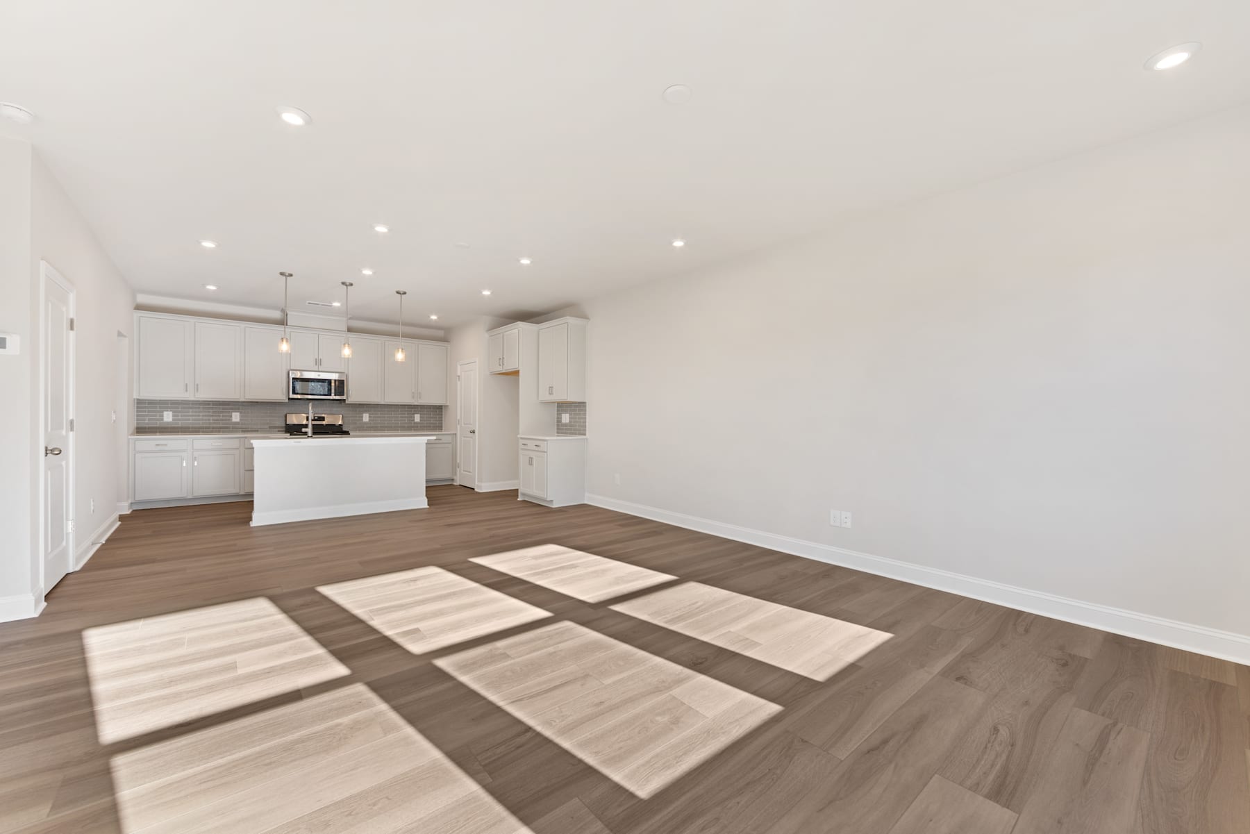 A modern, open-concept kitchen and living space with white walls, hardwood flooring, and recessed lighting.