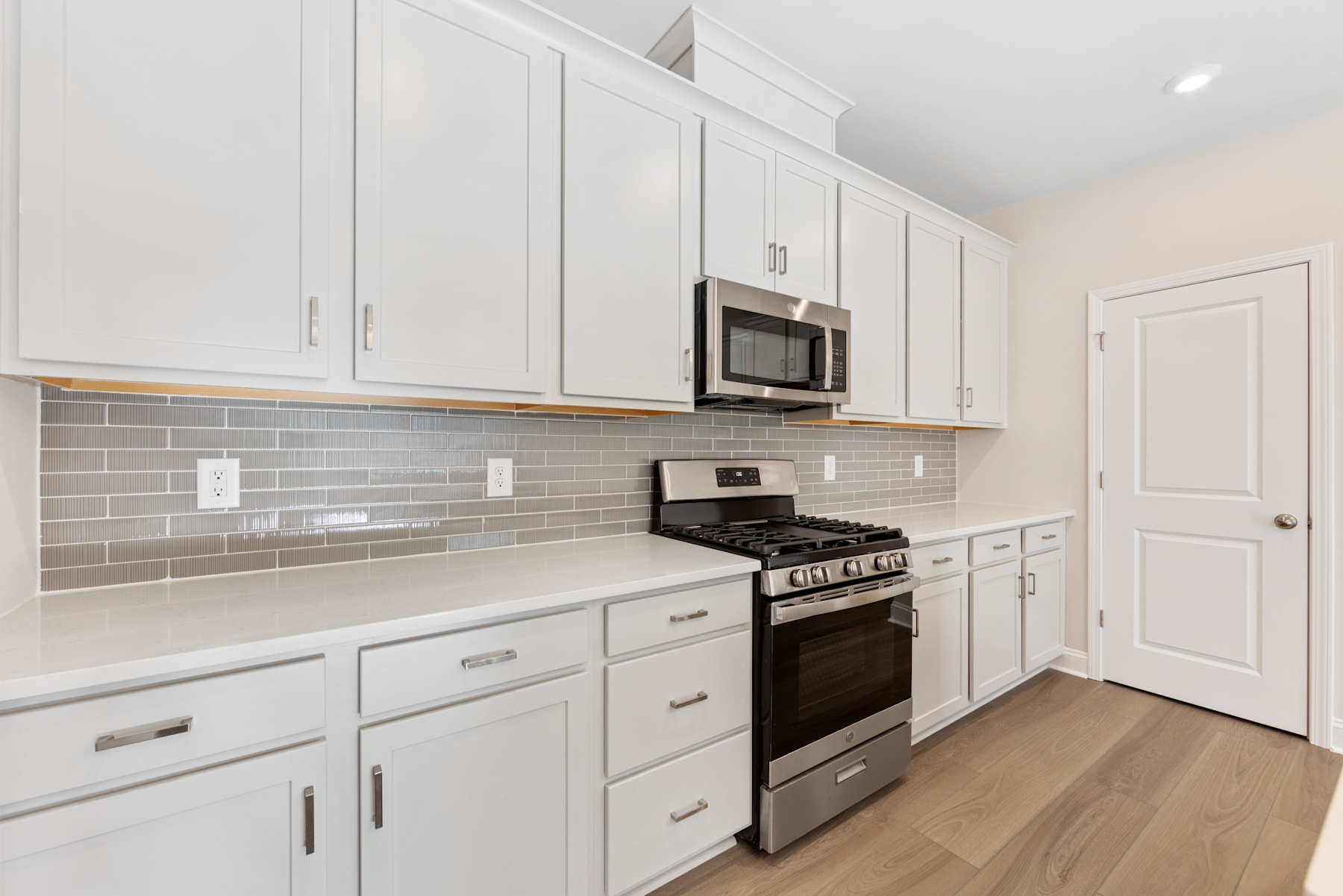 A modern, well-equipped kitchen with white cabinets, a gas stove, and a subway tile backsplash, set against a hardwood floor.