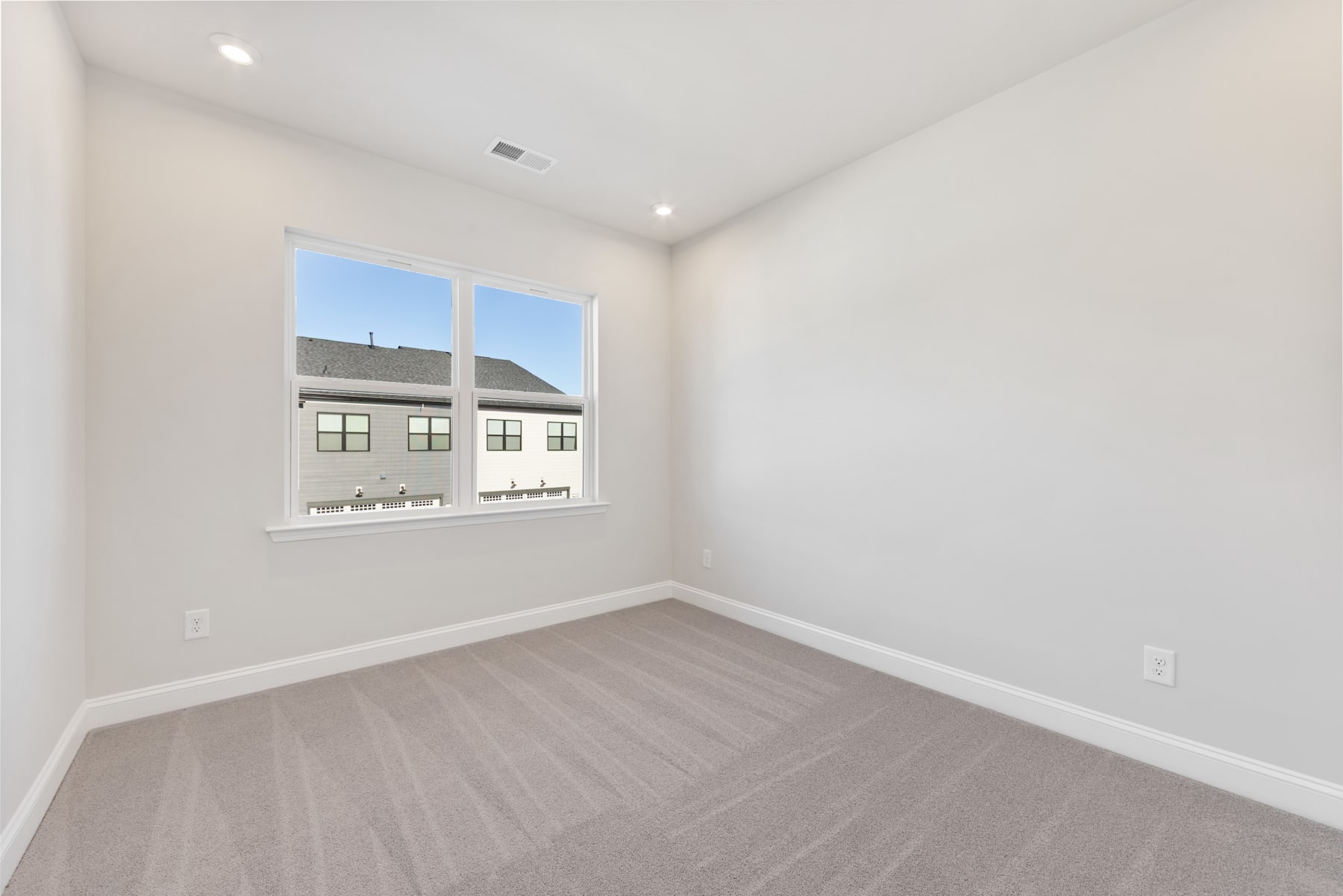 A bright, empty room with white walls, a large window, and a hardwood floor.