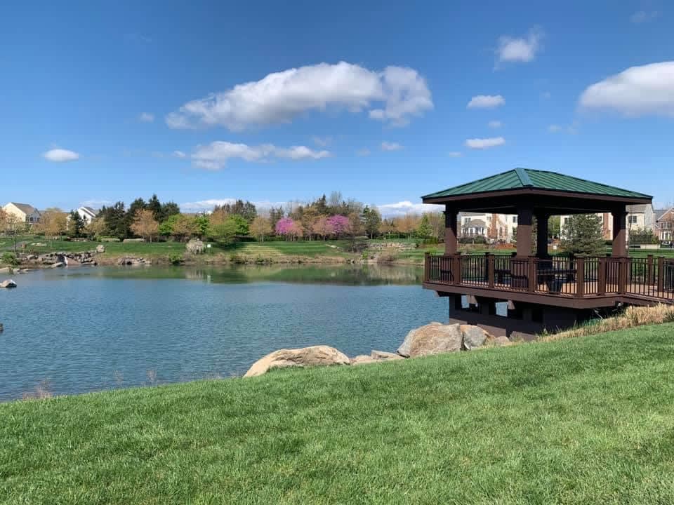 A serene pond surrounded by lush greenery, with a wooden gazebo overlooking the tranquil waters and a picturesque landscape in the background.