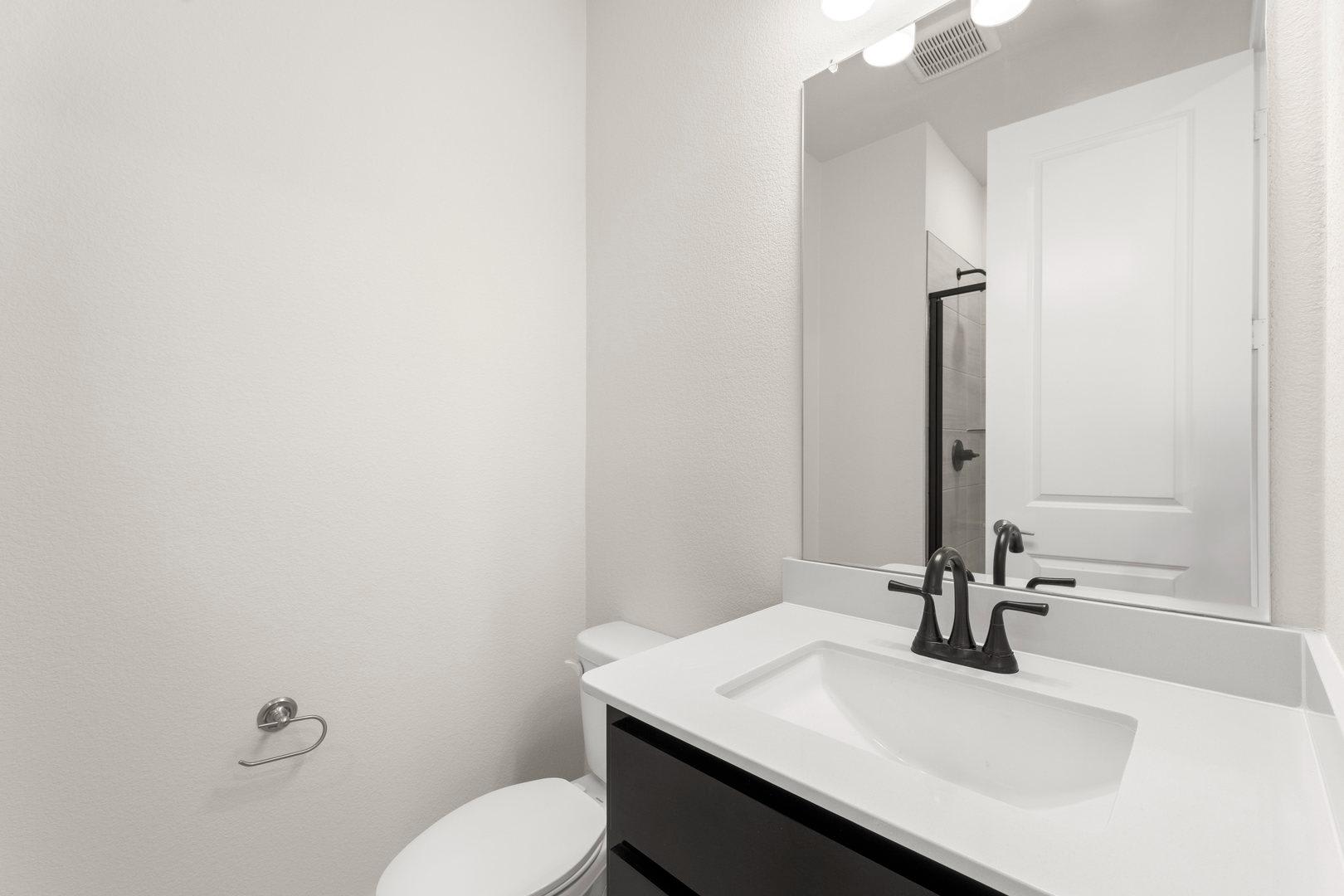 A modern, minimalist bathroom with a white sink, black faucet, and a large mirror on the wall.