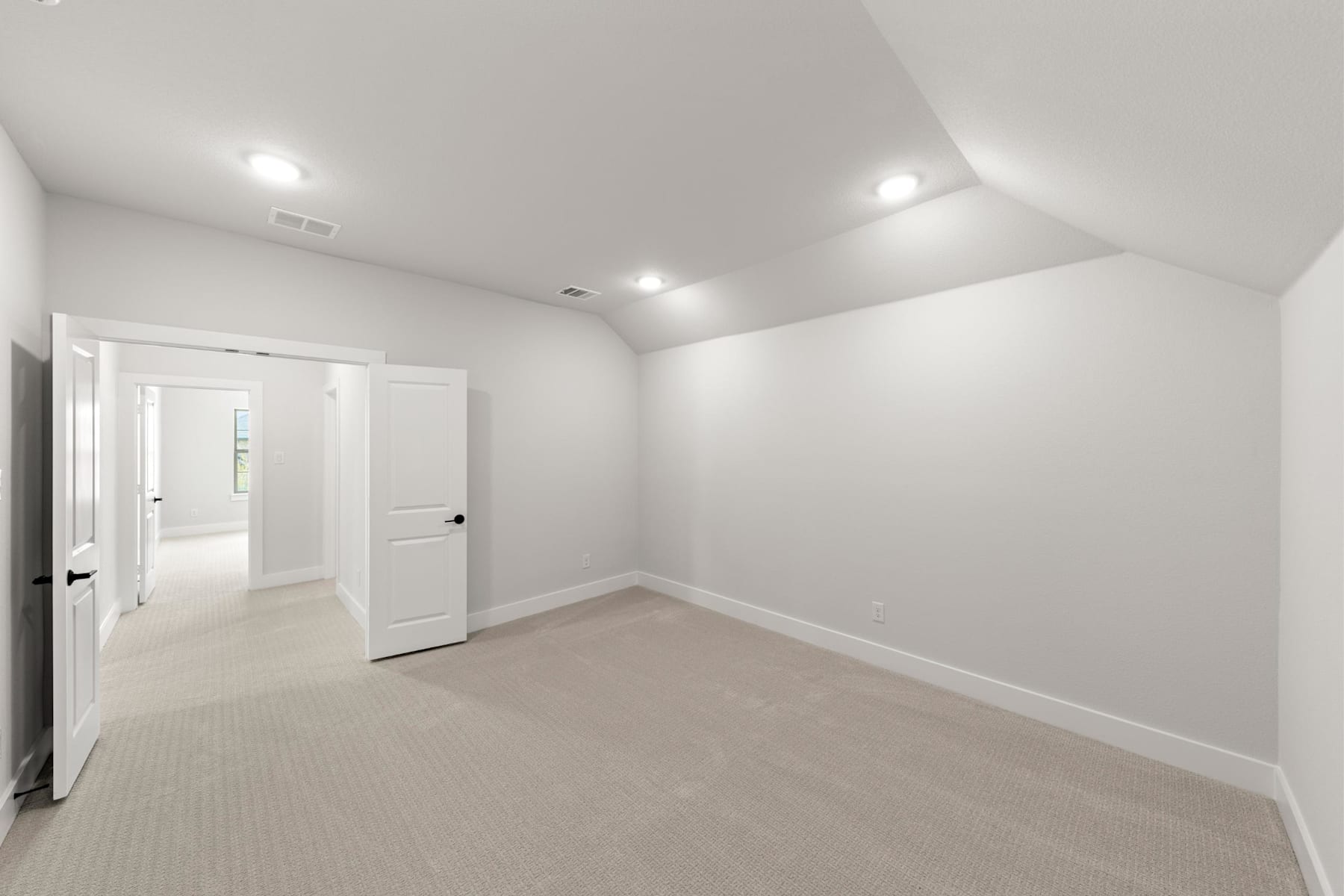 A spacious, well-lit room with white walls, a carpeted floor, and a doorway leading to another room.