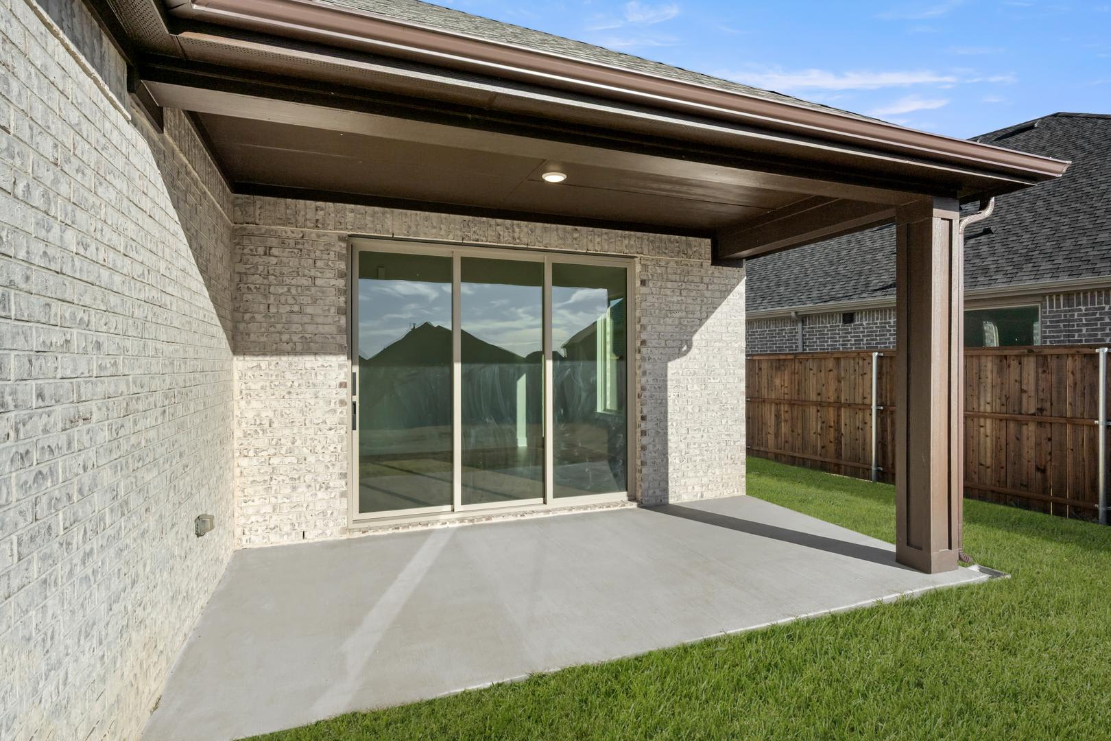 A modern, single-story house with a covered patio, surrounded by a well-manicured lawn and a wooden fence in the background.