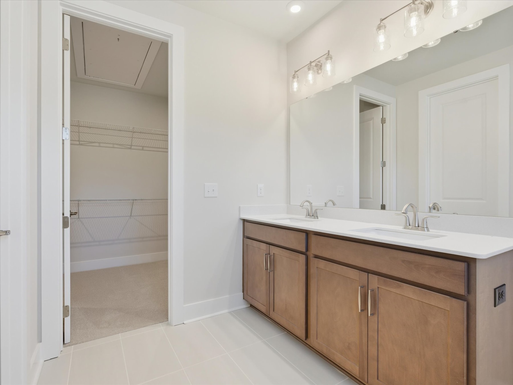 A spacious bathroom with a wooden vanity, white countertop, and a doorway leading to another room.