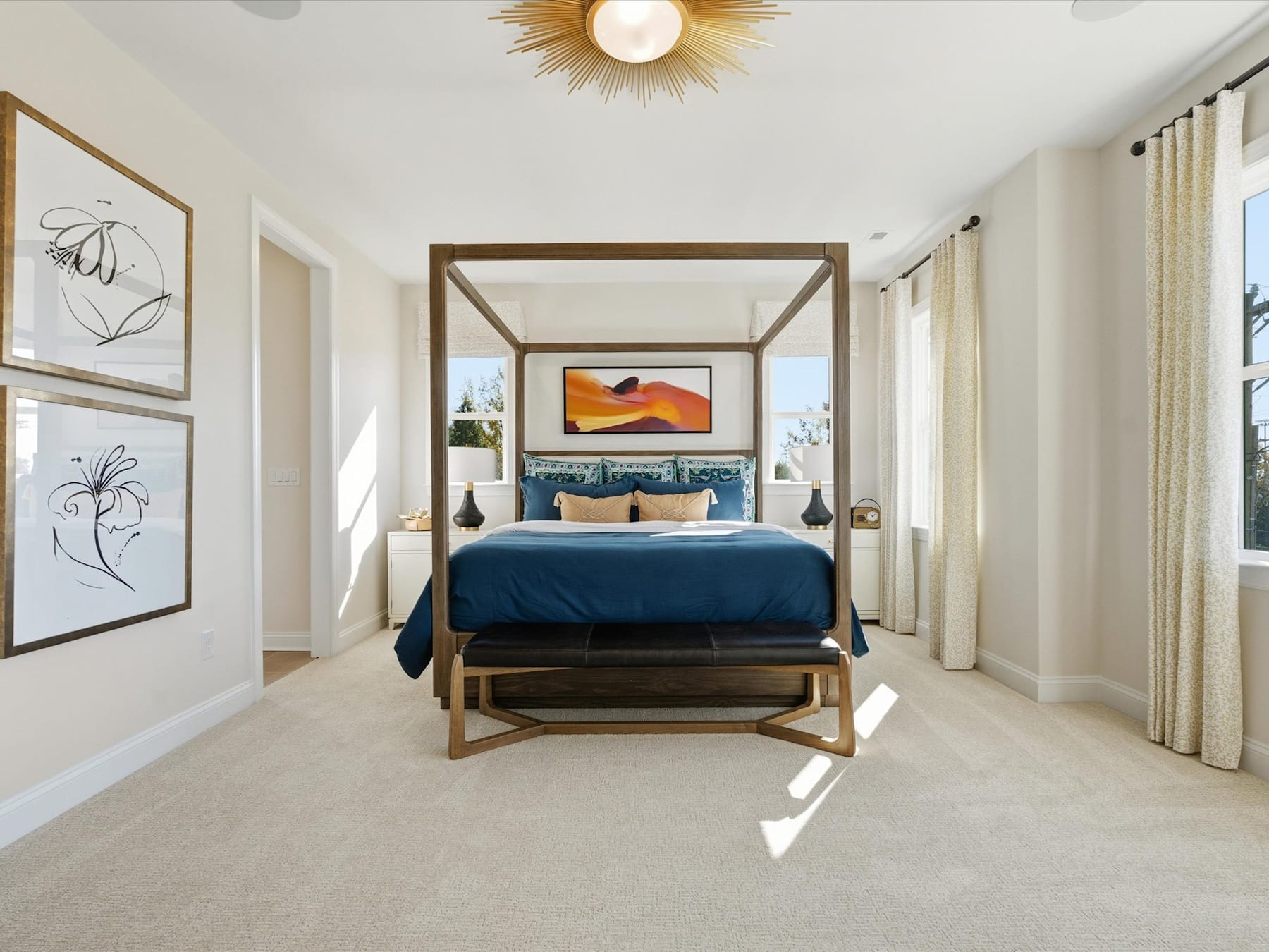 A spacious and well-designed bedroom with a large bed, wooden furniture, and artwork on the walls, illuminated by a modern light fixture.