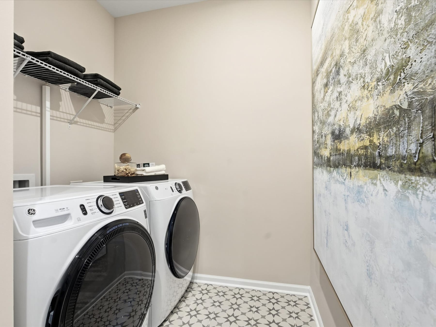 A modern laundry room with a white washer and dryer set against a wall with a large abstract painting.