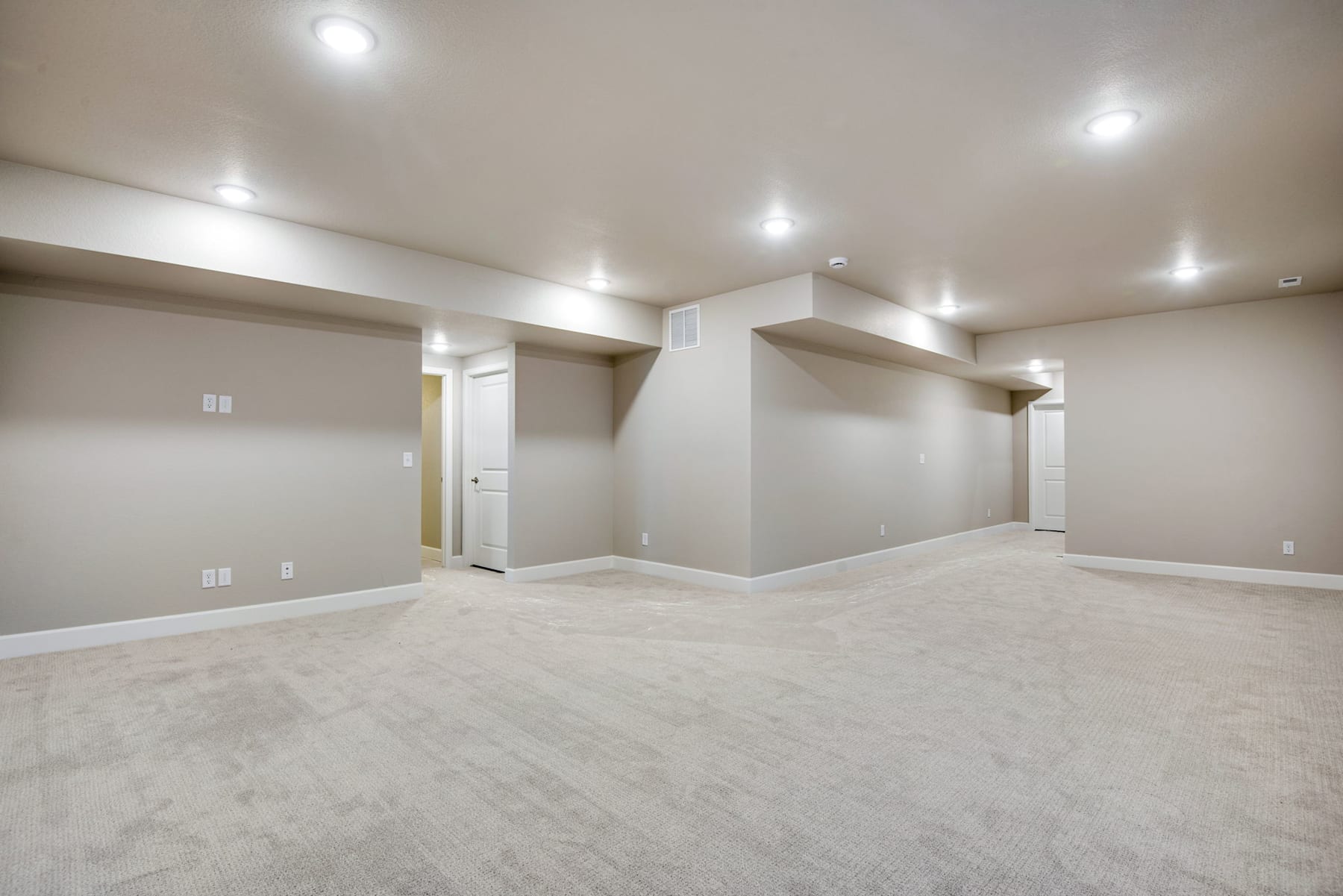 A spacious, well-lit room with a clean, minimalist design featuring white walls, recessed lighting, and a smooth, light-colored floor.