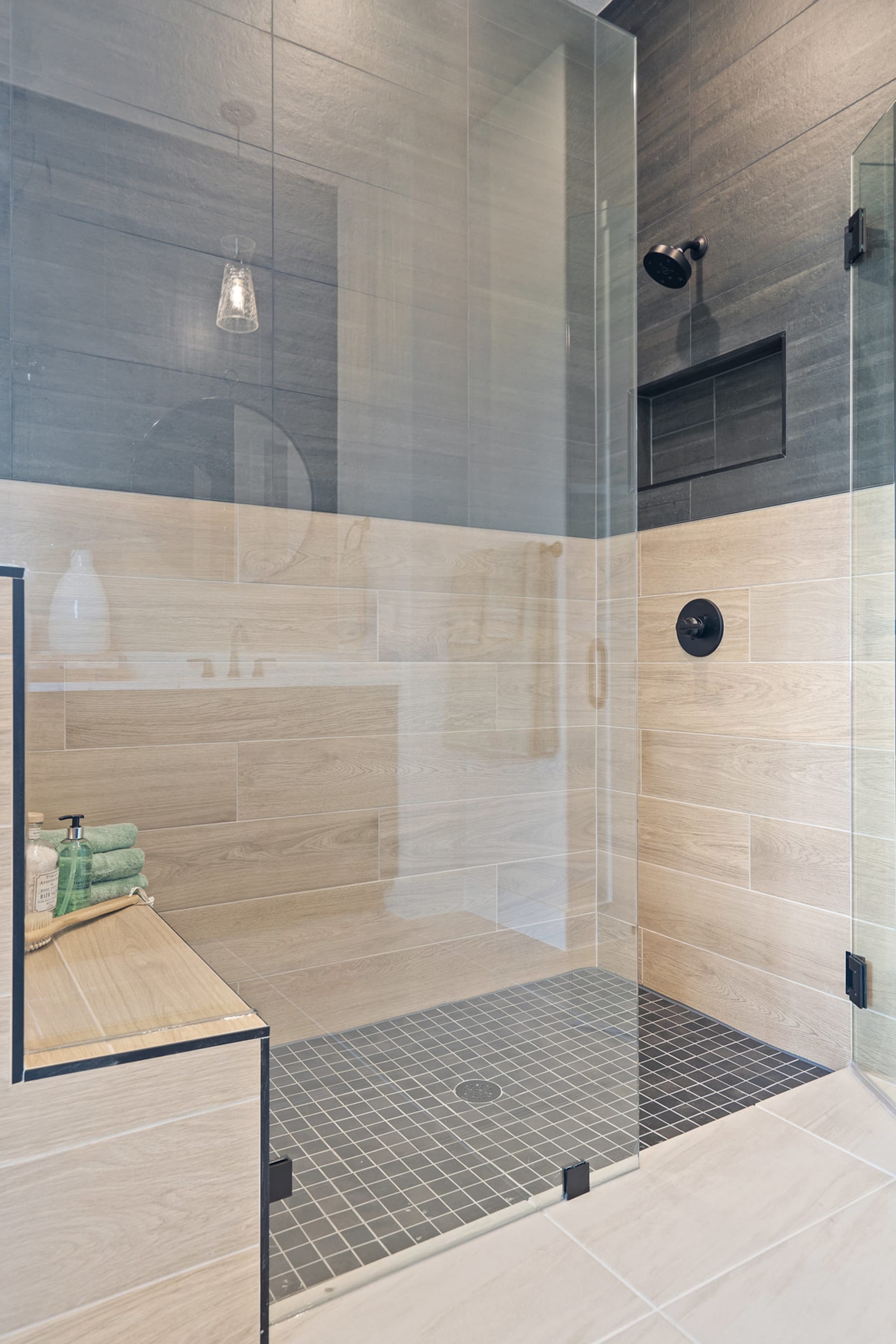 A modern, tiled bathroom with a glass-enclosed shower area, a bench, and a mirror on the wall.