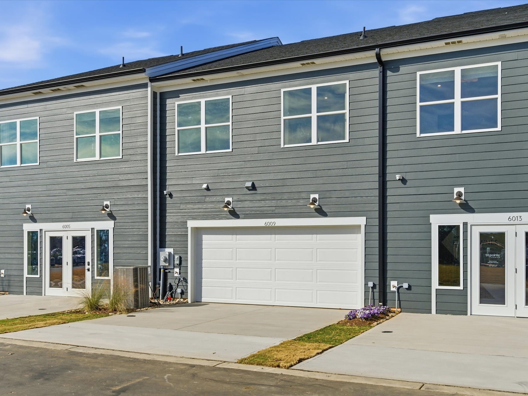 A row of modern, gray townhouses with white garage doors and front entrances, set against a clear blue sky.