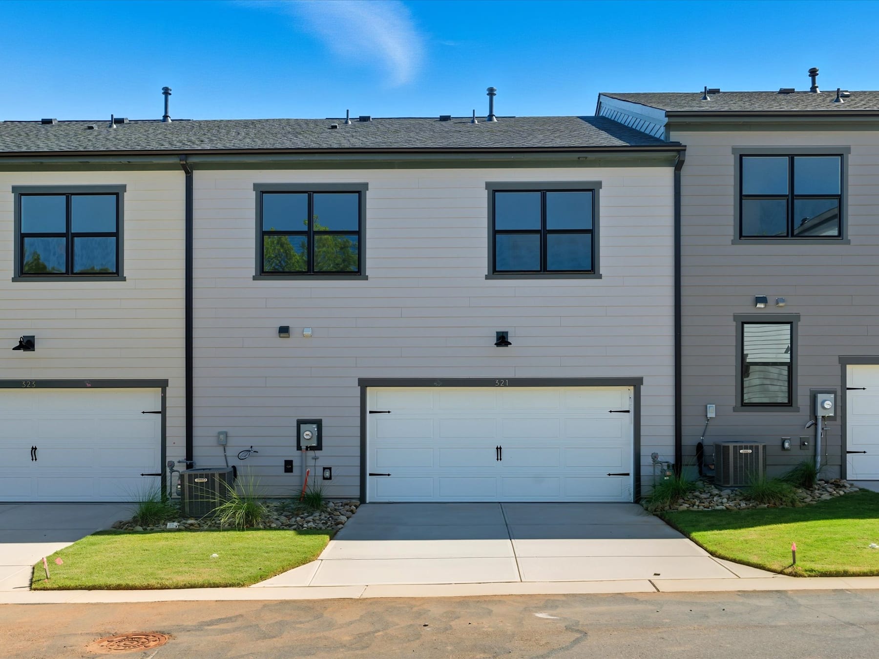A modern townhouse with a gray exterior, featuring multiple windows and a garage door in the foreground, set against a clear blue sky in the background.
