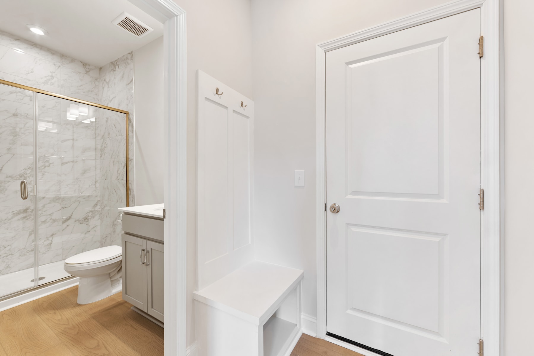A bright and spacious bathroom with a white marble-tiled shower enclosure, a vanity cabinet, and a closed white door leading to another room.
