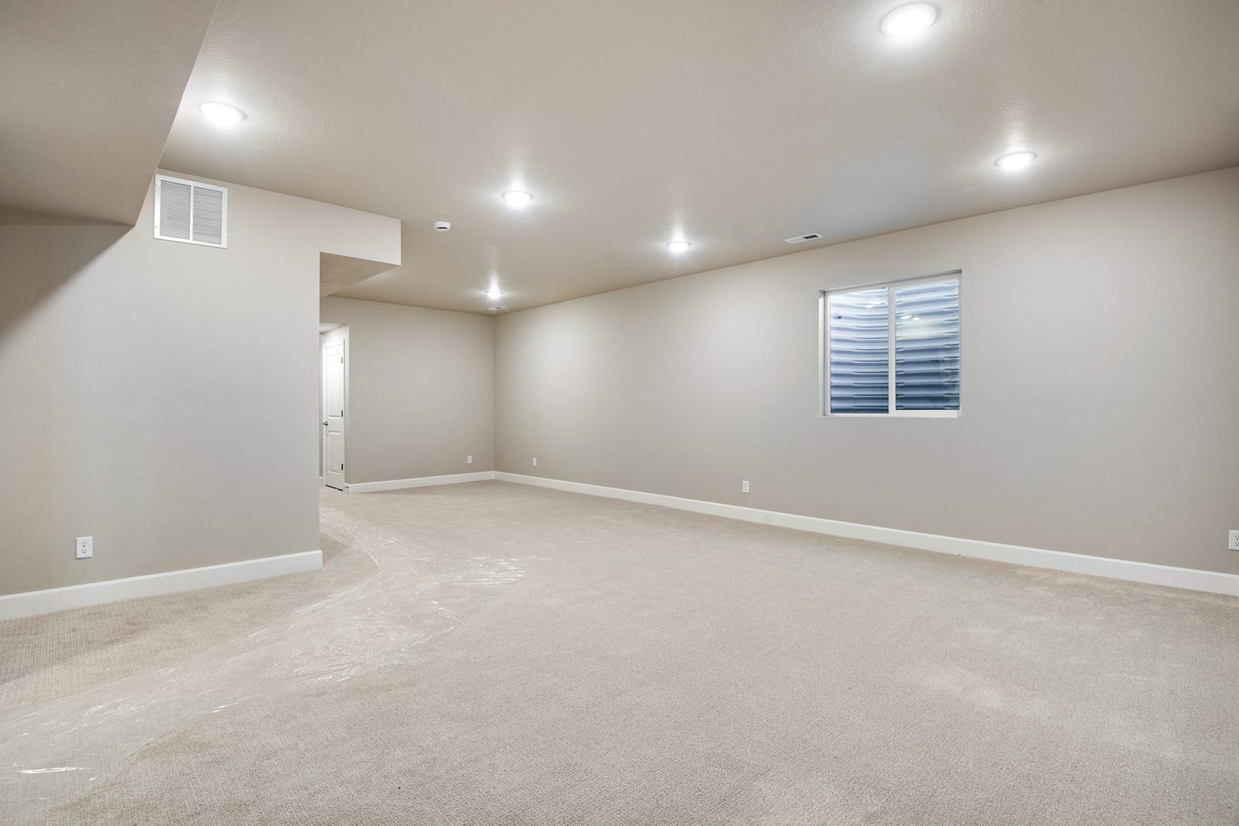 A spacious, well-lit room with a clean, carpeted floor and recessed lighting in the ceiling.