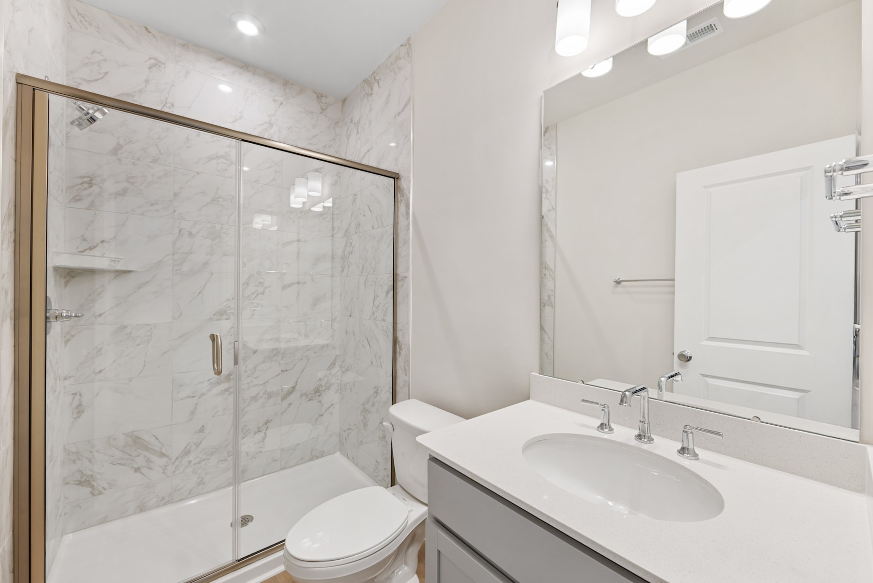 A modern, minimalist bathroom with a marble-tiled shower enclosure, a white vanity with a sink, and a large mirror on the wall.