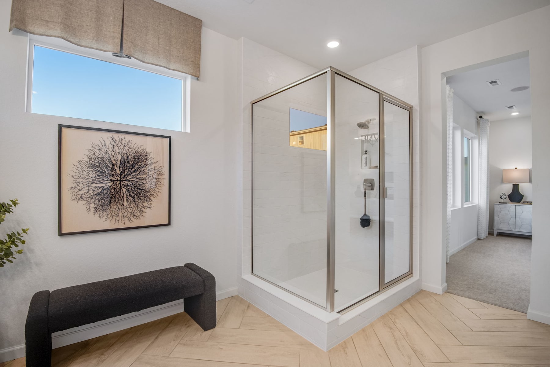 A modern and minimalist entryway with a glass-enclosed shower, a framed artwork on the wall, and a wooden bench in the foreground.