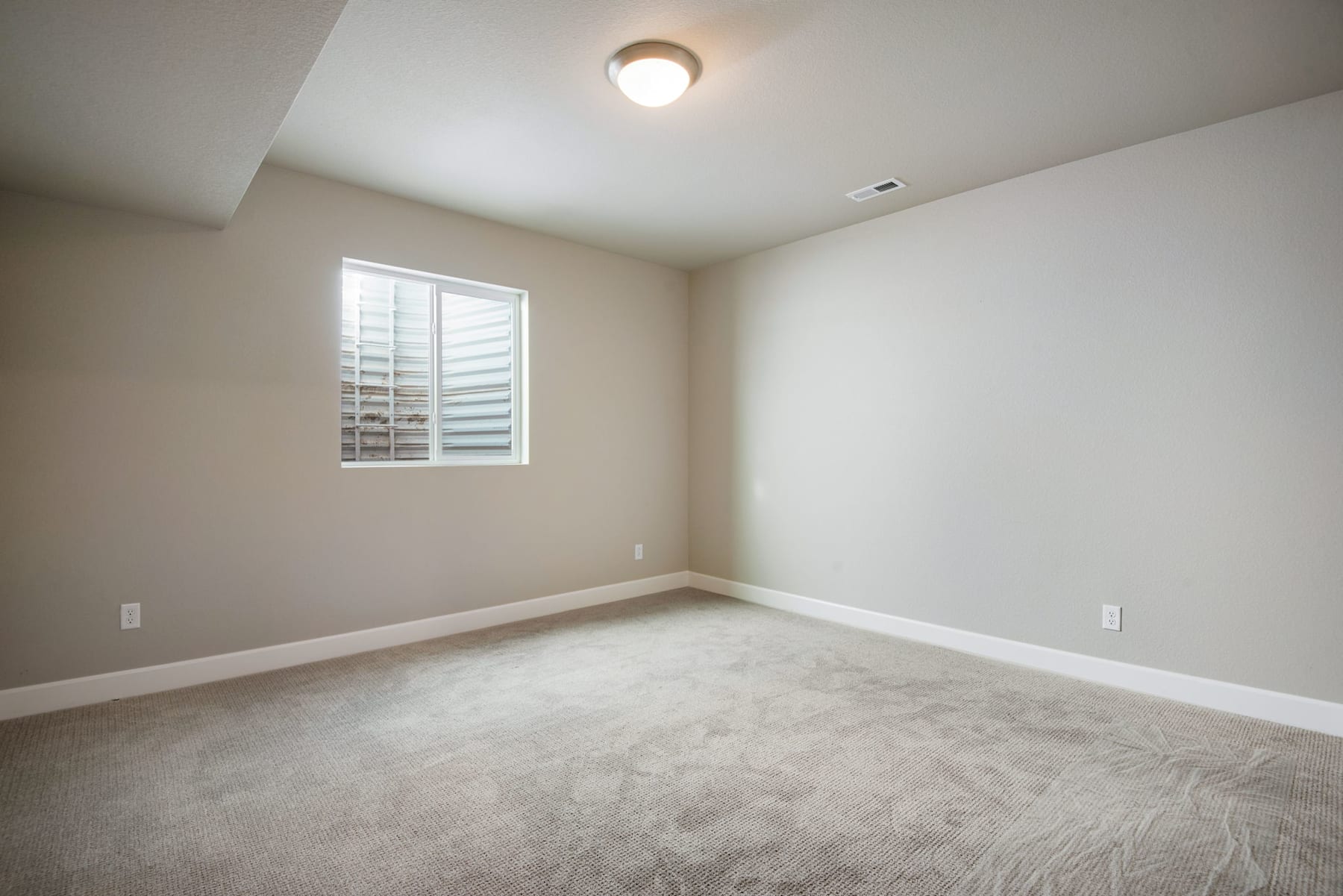 A spacious, well-lit room with a window, a ceiling light, and a carpeted floor.