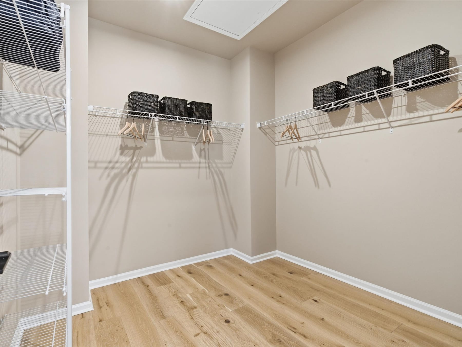 A spacious walk-in closet with wooden flooring, wire shelves, and a hanging rod for clothes.