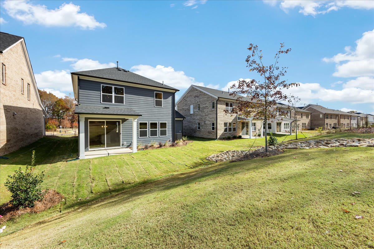 A residential neighborhood with well-maintained homes, lush green lawns, and a clear blue sky with scattered clouds in the background.