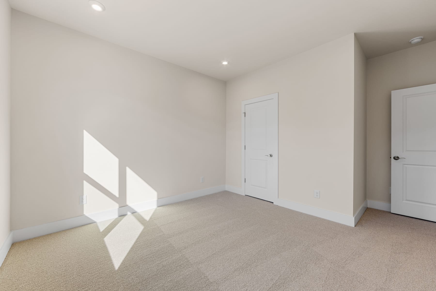 An empty, well-lit room with white walls, a carpeted floor, and two closed doors visible.
