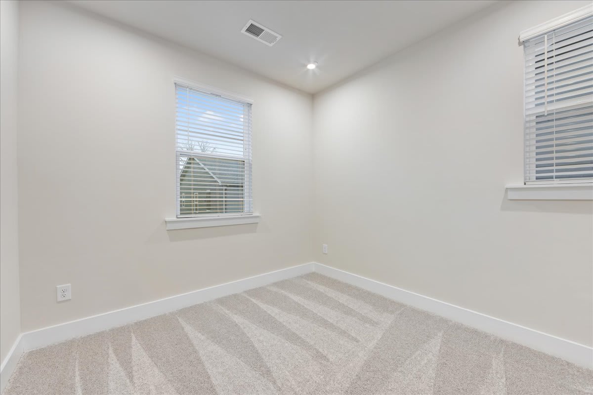 A bright, empty room with white walls, a window, and a light-colored carpet covering the floor.
