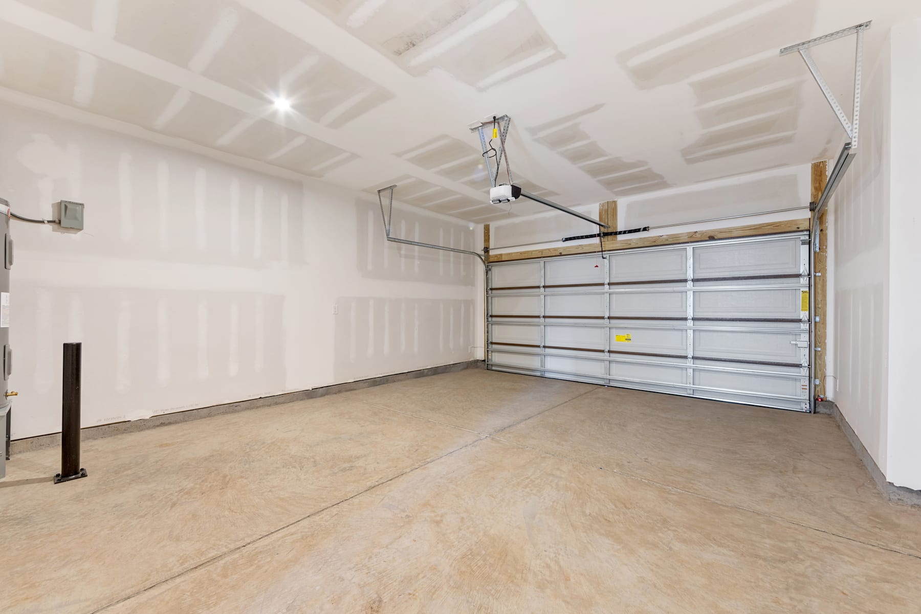 A spacious and well-lit garage interior with a concrete floor, a large garage door, and various storage shelves and fixtures.