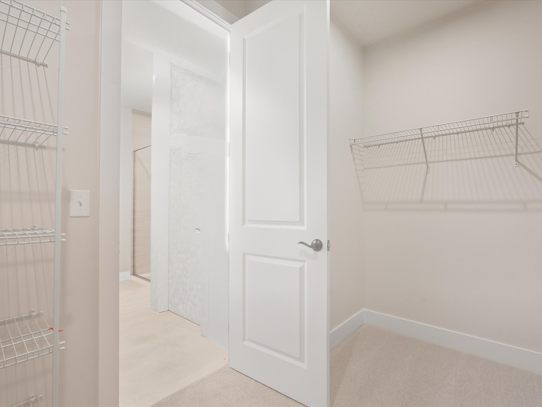 A bright, minimalist laundry room with white walls, a closed door, and wire shelving units on the walls.