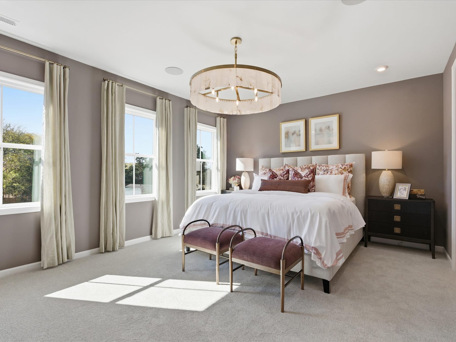 A spacious and elegantly decorated bedroom with a large bed, plush bedding, and a stylish chandelier overhead, surrounded by large windows that allow natural light to flood the room.