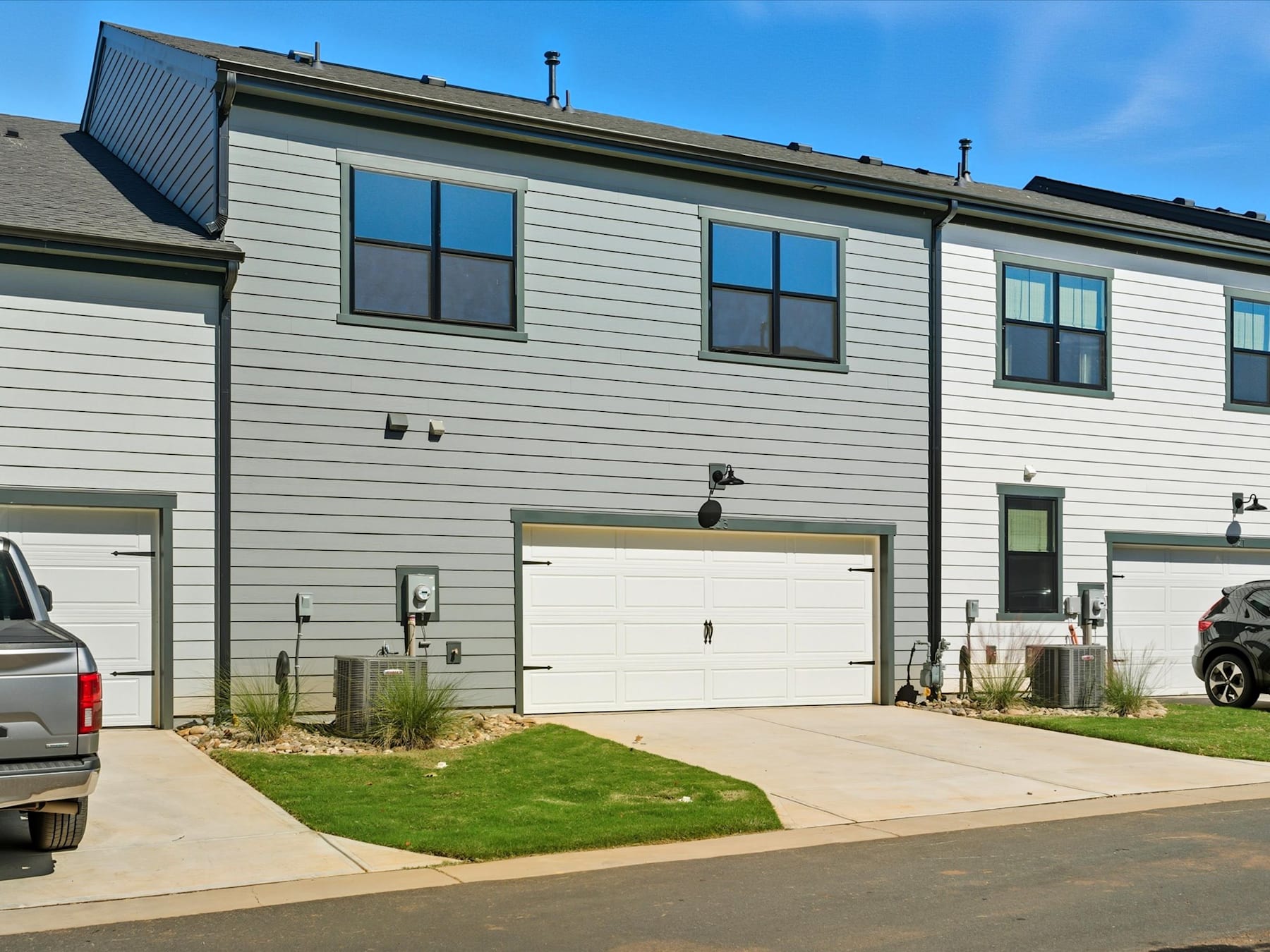 A modern, multi-unit residential building with a gray exterior, a paved driveway, and a well-maintained lawn in the foreground.