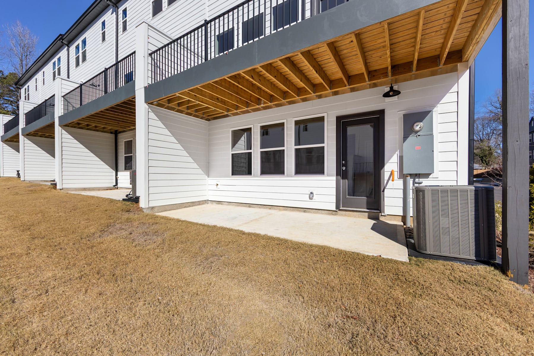 A white multi-story building with a wooden overhang and a paved walkway leading to the entrance, surrounded by a grassy area.