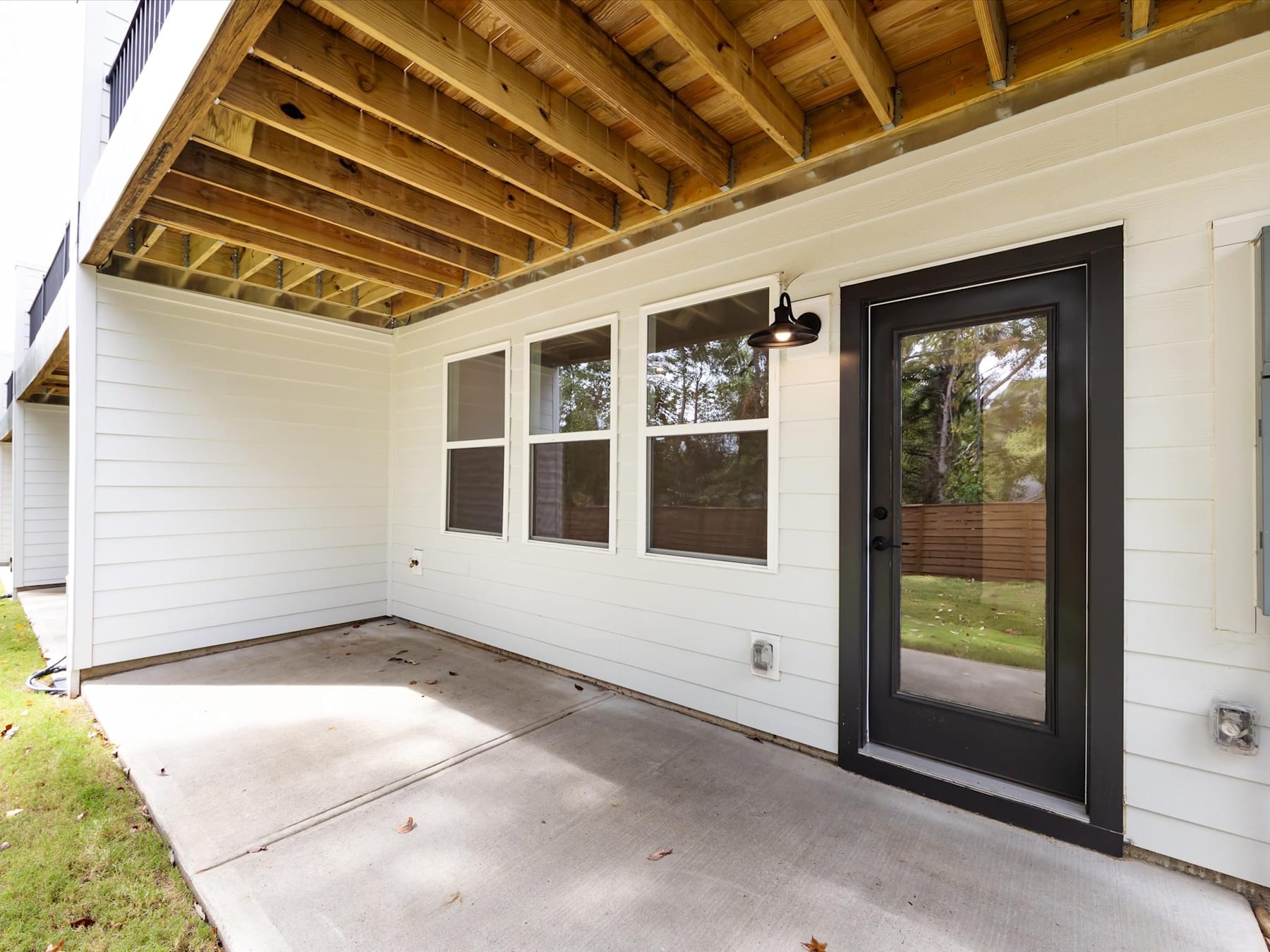 The image shows a covered porch with a wooden ceiling and large windows, leading out to a grassy yard.