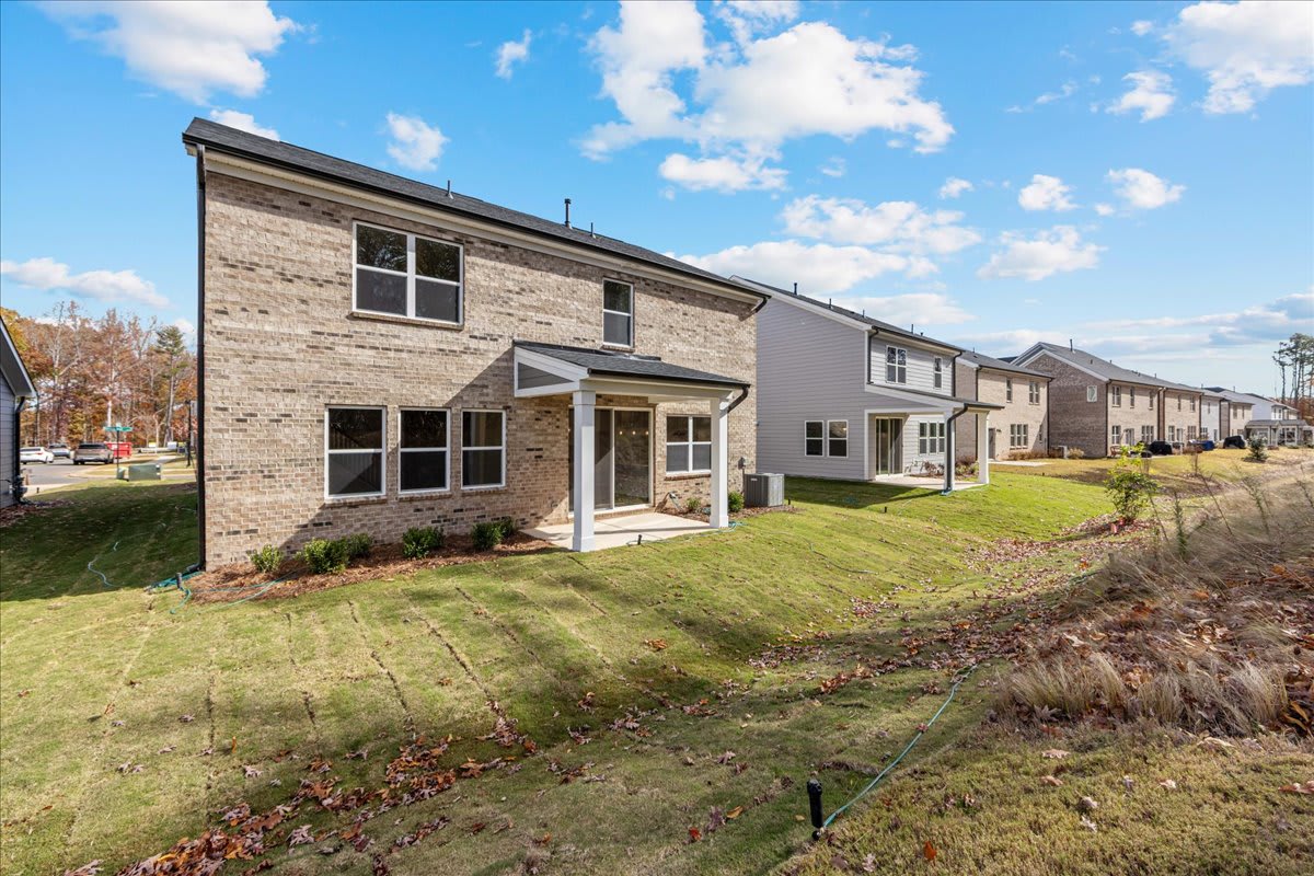 A row of modern, brick-clad townhouses with well-manicured lawns and a clear blue sky with fluffy clouds in the background.