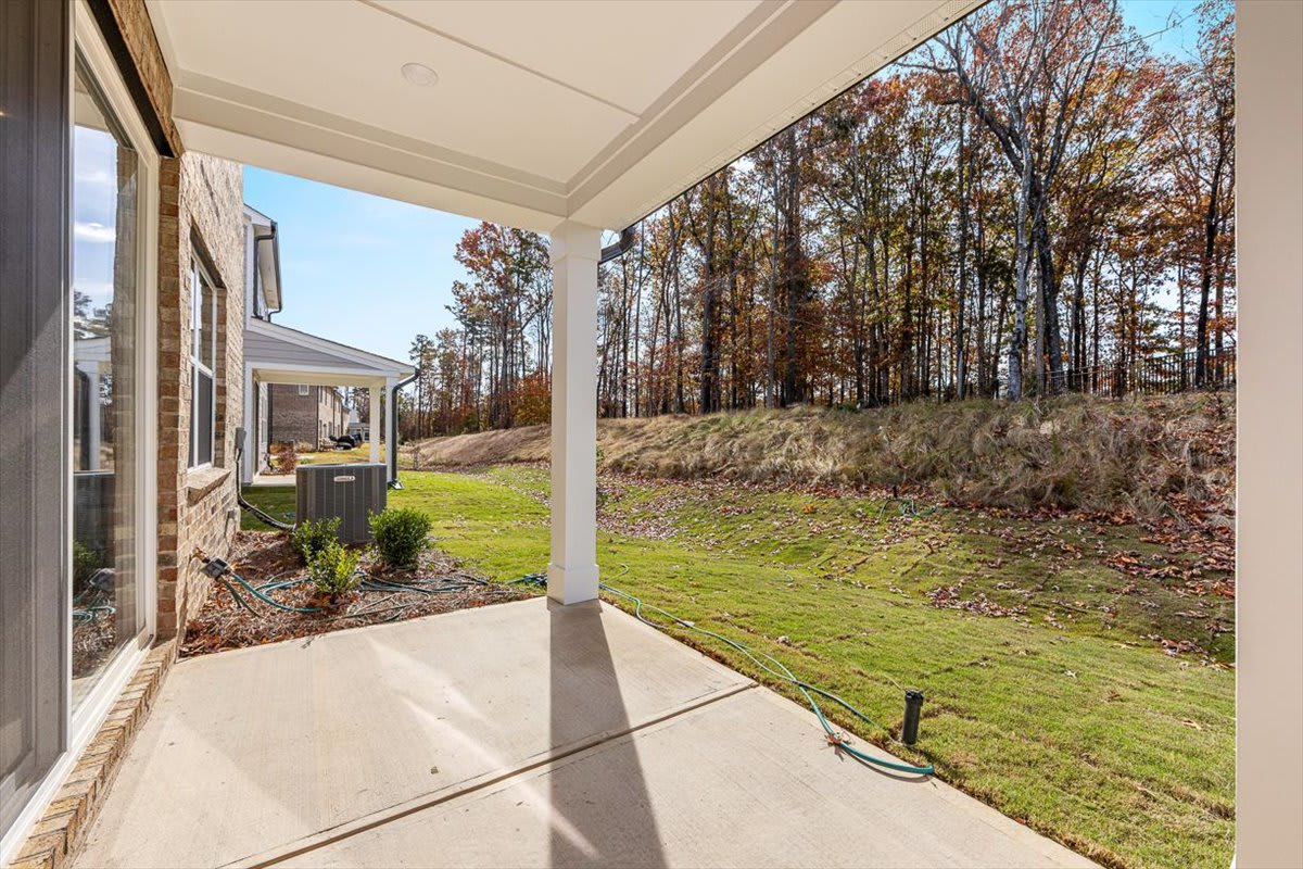A covered porch leads to a grassy yard surrounded by a wooded area with trees in autumn foliage.
