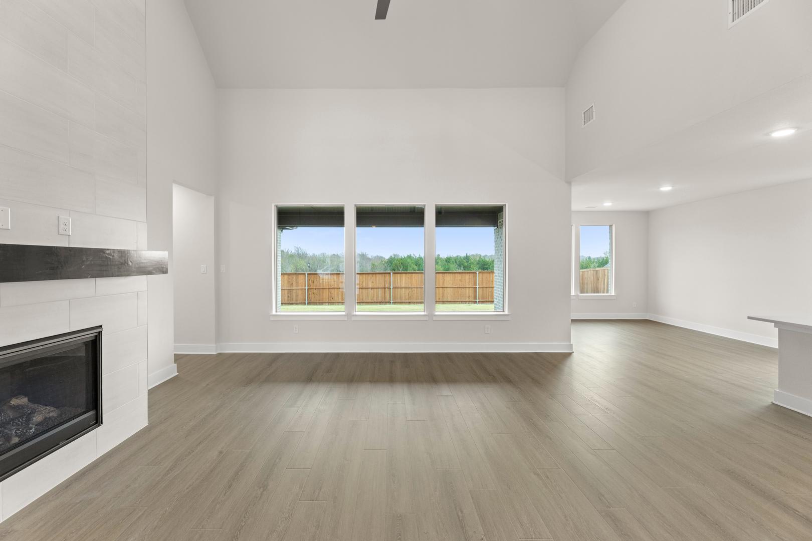 A spacious, bright room with a fireplace and large windows overlooking a fenced backyard.