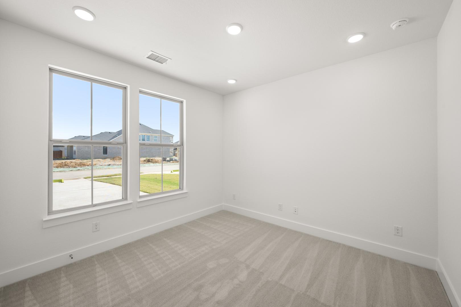 A bright, empty room with large windows overlooking a grassy outdoor area.