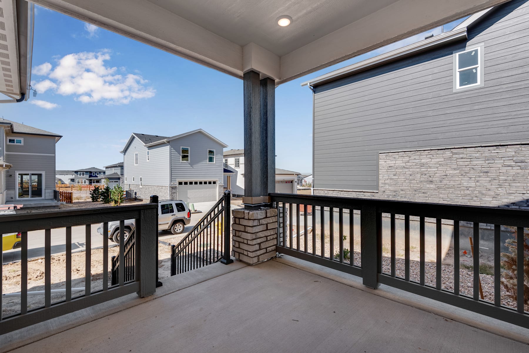 A balcony with a metal railing overlooks a residential neighborhood with houses and a cloudy blue sky in the background.