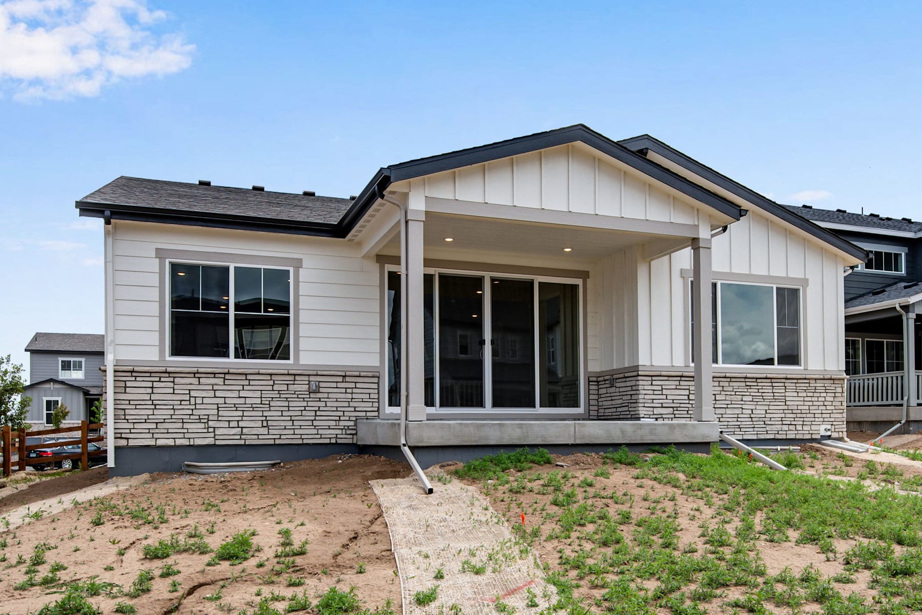 A newly constructed single-story house with a porch, surrounded by a grassy yard and a clear blue sky in the background.