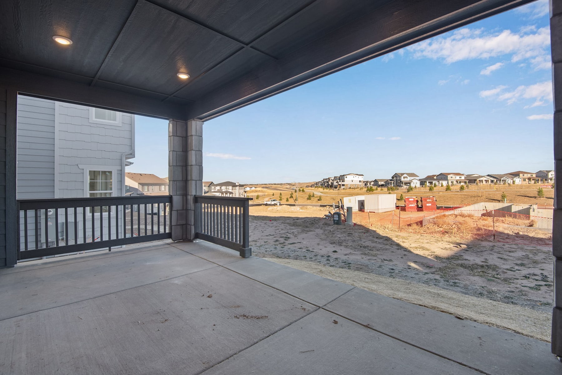 A covered porch overlooking a construction site with partially built houses in the background, set against a bright, cloudy sky.