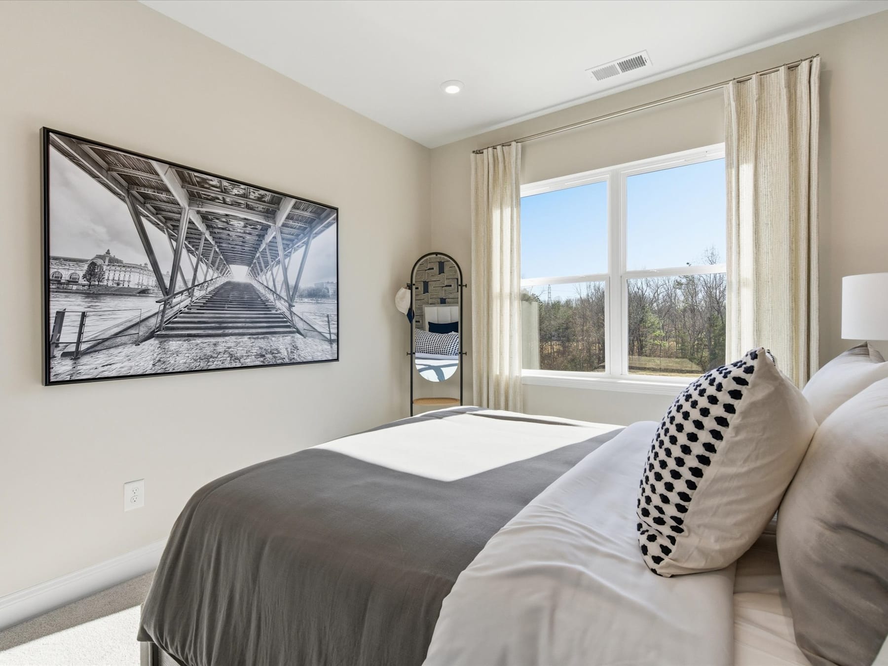 A modern and cozy bedroom with a large window overlooking a scenic outdoor landscape, featuring a black and white framed artwork on the wall.