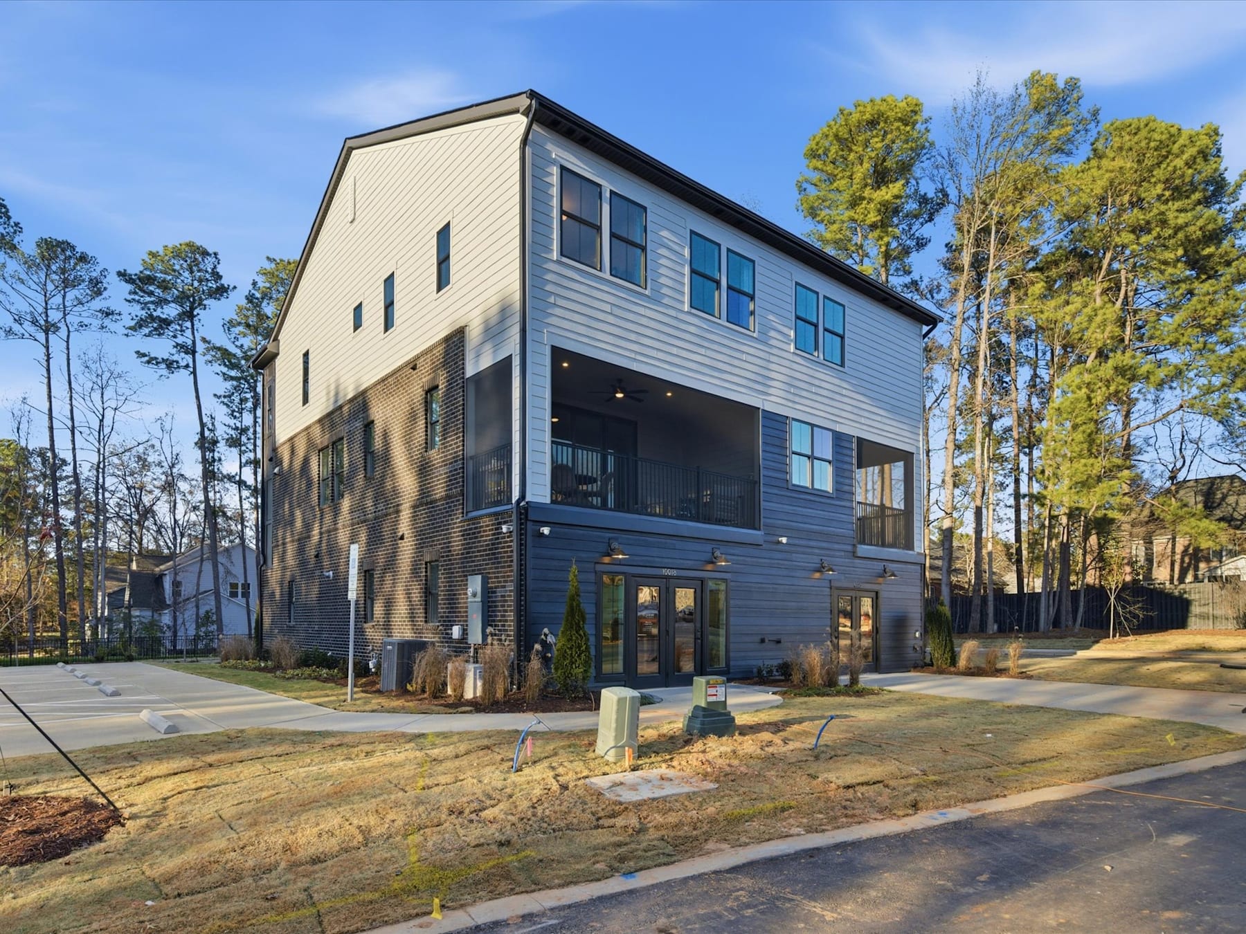 A modern, multi-story residential building with a mix of wood and glass exterior stands in a wooded area, surrounded by trees and a grassy lawn in the foreground.