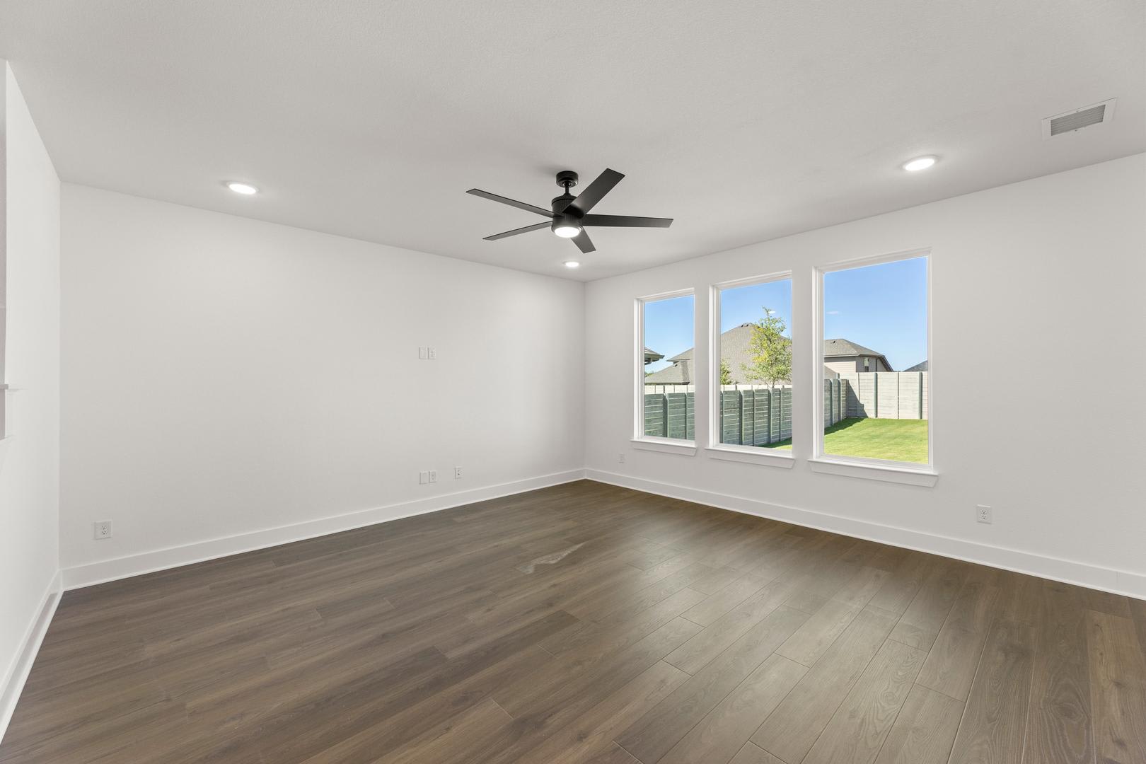 A spacious, well-lit room with a ceiling fan and large windows overlooking a grassy outdoor area.