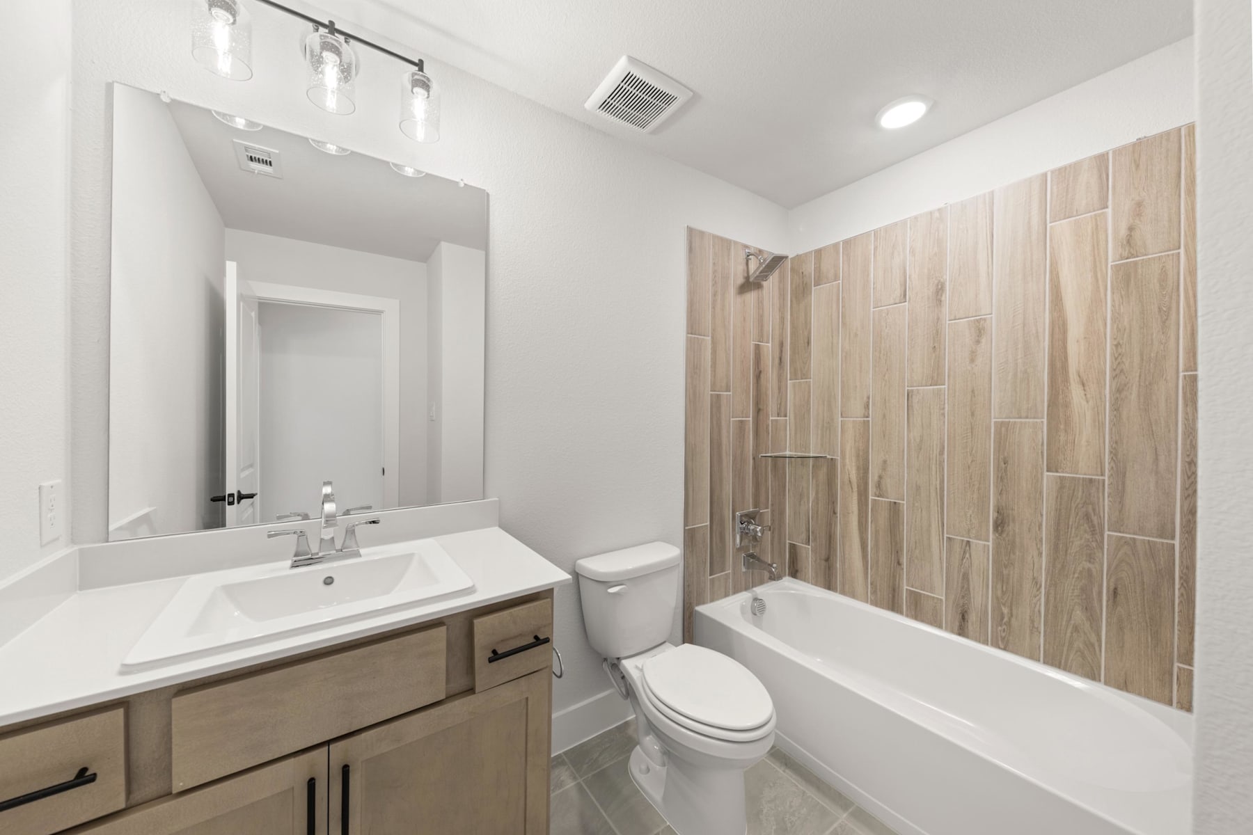 A modern and minimalist bathroom with a white vanity, a large mirror, and a tiled shower enclosure.