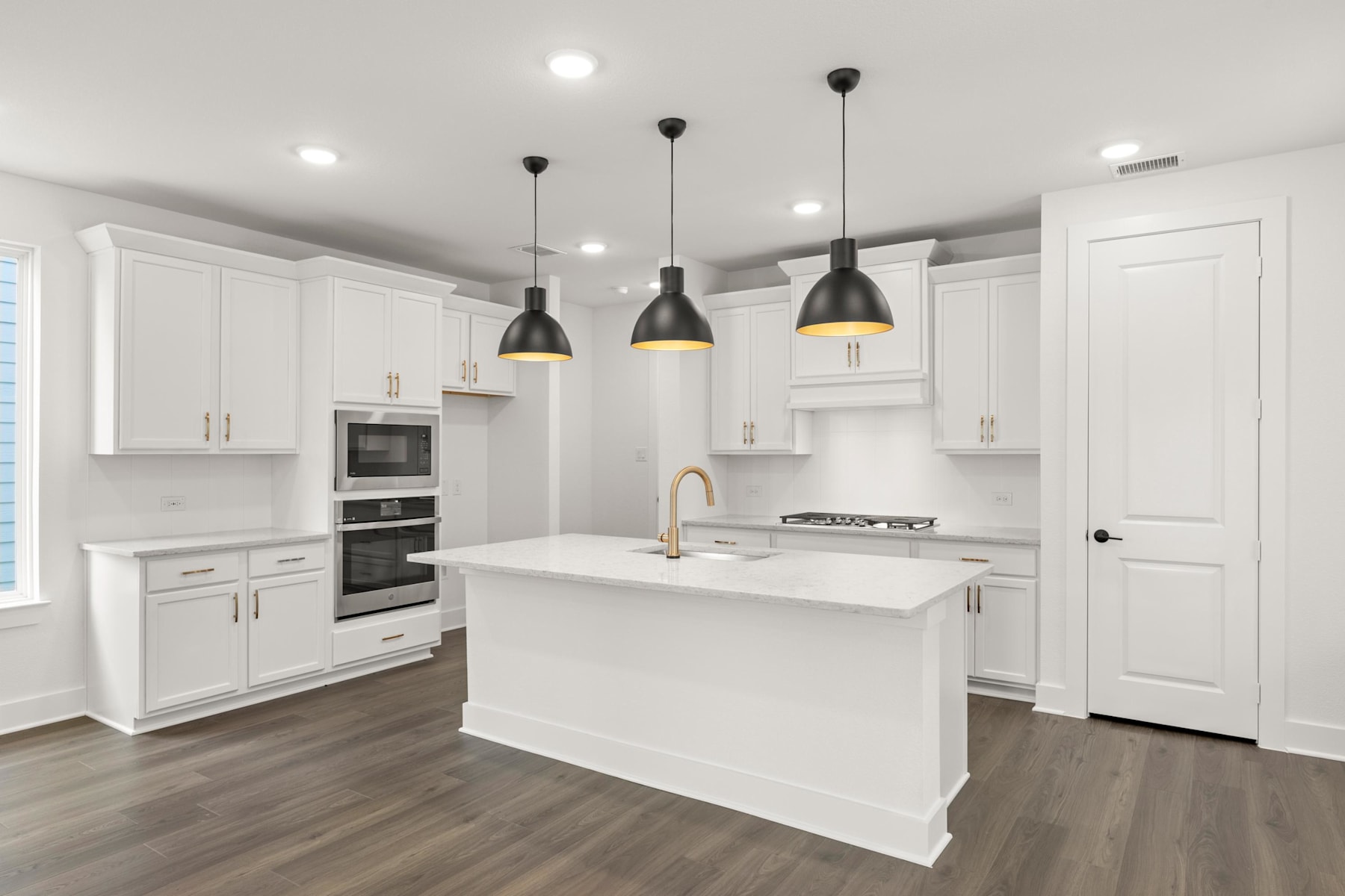 A modern, bright kitchen with white cabinets, a large island, and pendant lights hanging above, set against a hardwood floor.