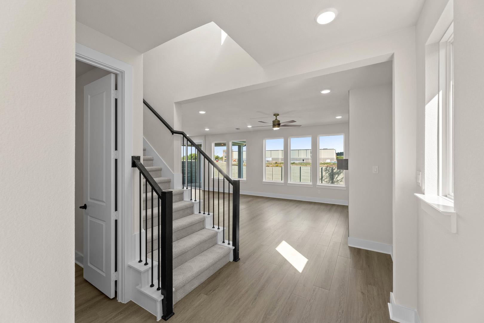 A bright and spacious interior with a staircase leading up to a second floor, featuring hardwood floors, white walls, and recessed lighting.