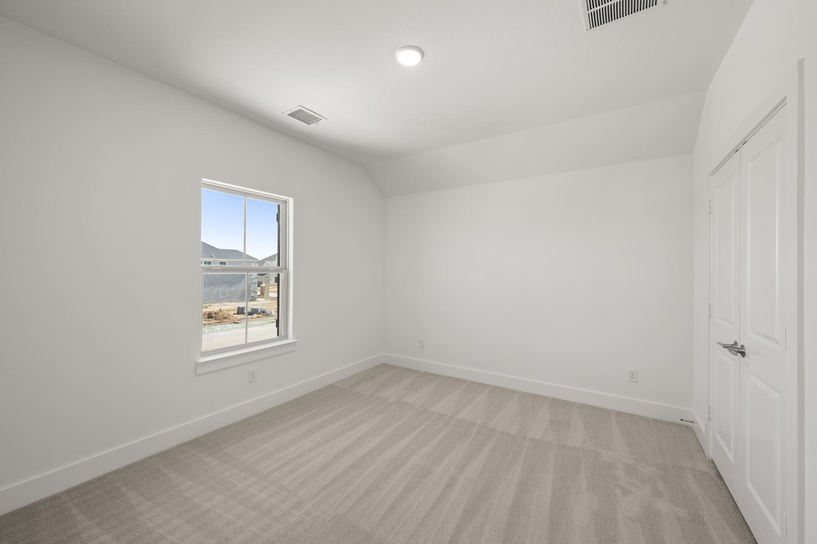 A bright, empty room with a window overlooking a landscape, featuring a hardwood floor and a single light fixture on the ceiling.