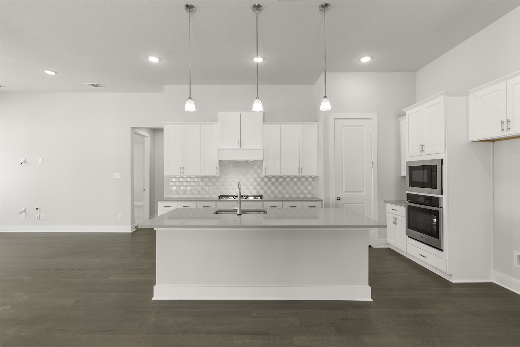 A modern, minimalist kitchen with white cabinets, stainless steel appliances, and pendant lighting fixtures suspended from the ceiling.