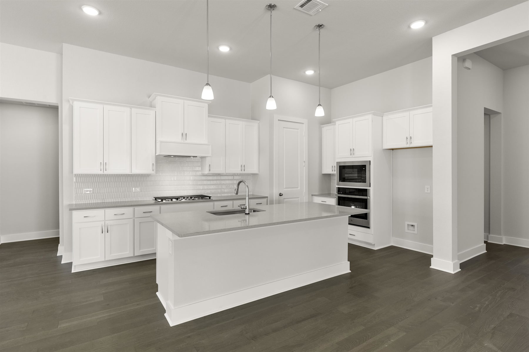 A modern, bright, and spacious kitchen with white cabinets, a central island, and dark hardwood floors.
